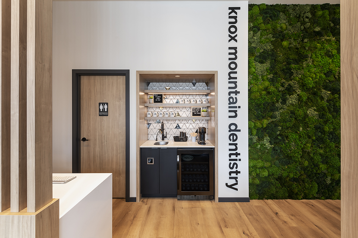 A dental reception area featuring a coffee station, a restroom door, and a green moss wall, with text that reads "knox mountain dentistry."