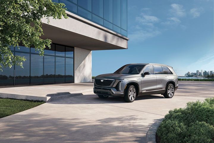 A sleek gray SUV parked in front of a modern building, surrounded by green landscaping and a clear blue sky.