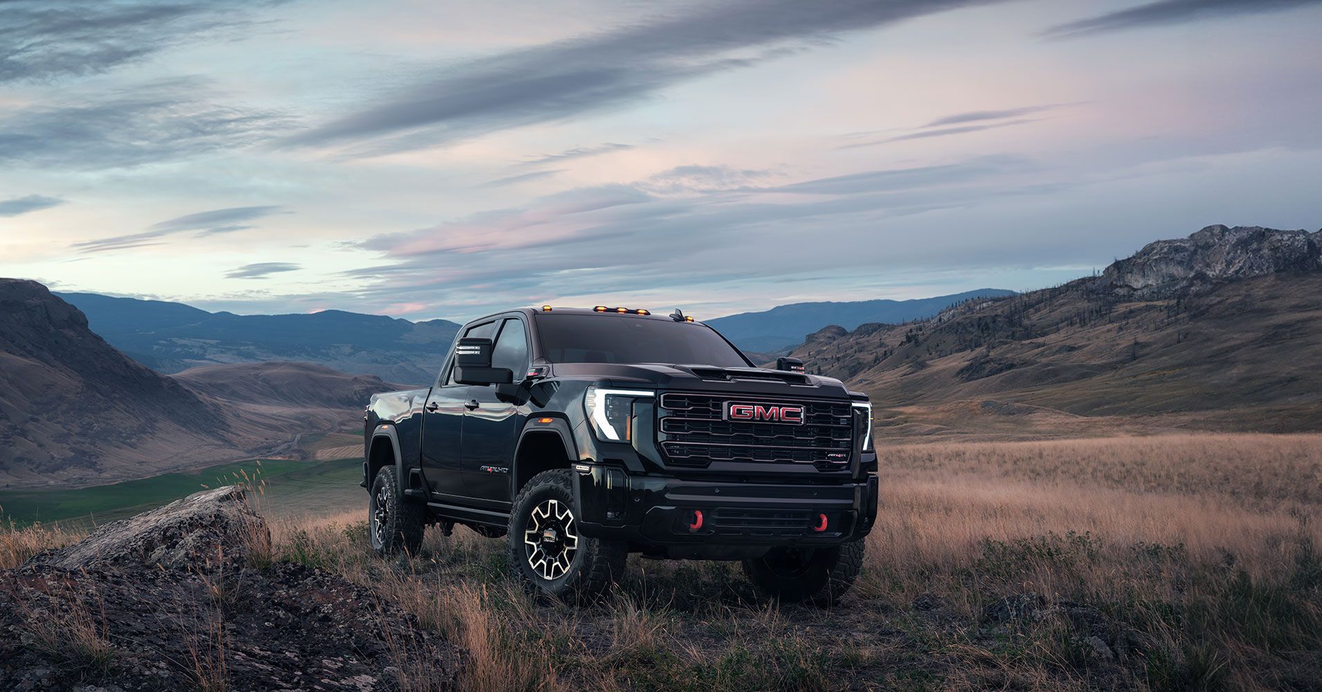 A black GMC pickup truck parked on a rocky landscape, with mountains and a cloudy sky in the background.