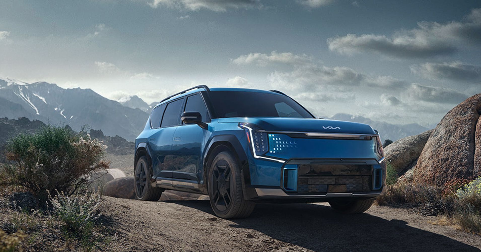 A blue SUV parked on a dirt road with mountains in the background.