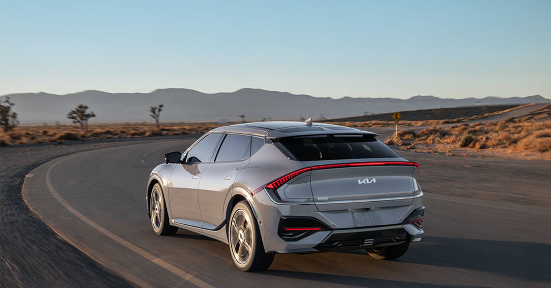 A silver electric car driving on a winding road in a desert landscape.