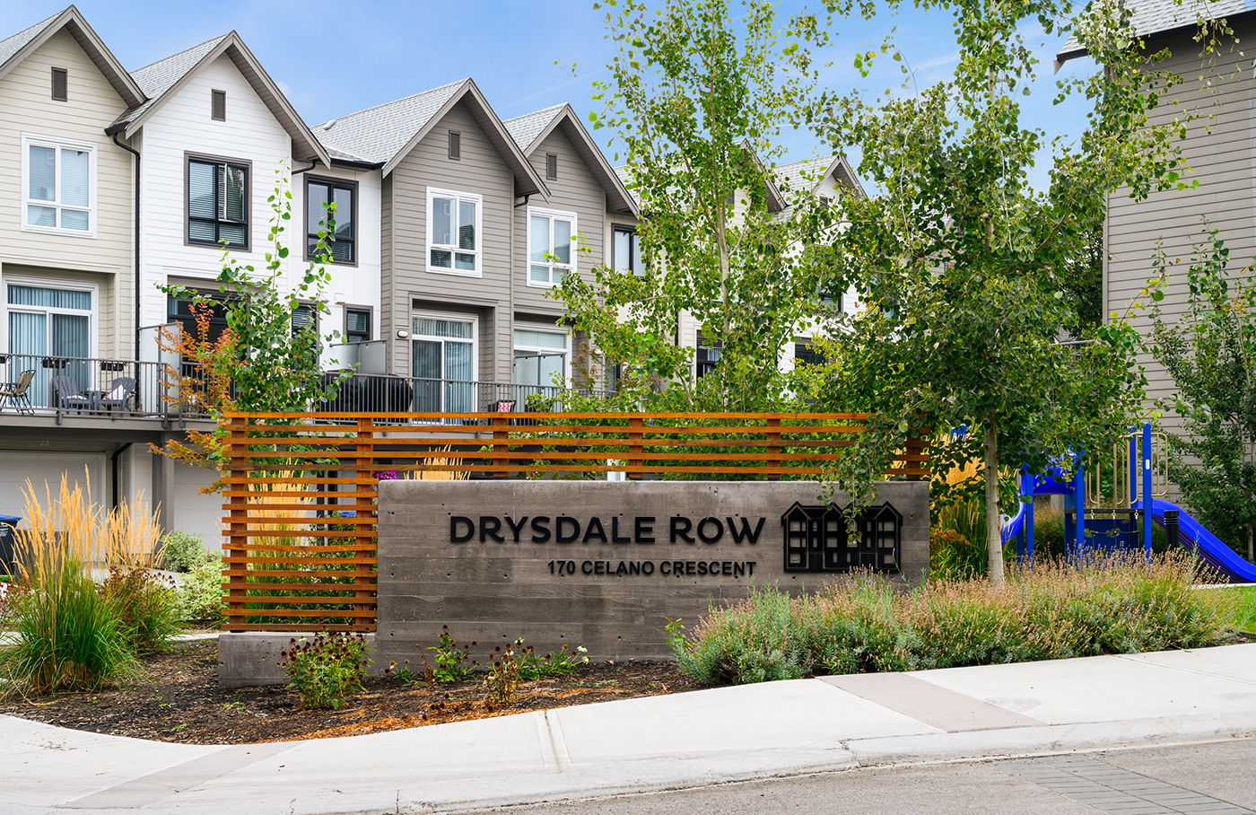 A sign for "Drysdale Row" at 170 Celano Crescent, surrounded by modern townhouses, greenery, and a playground.