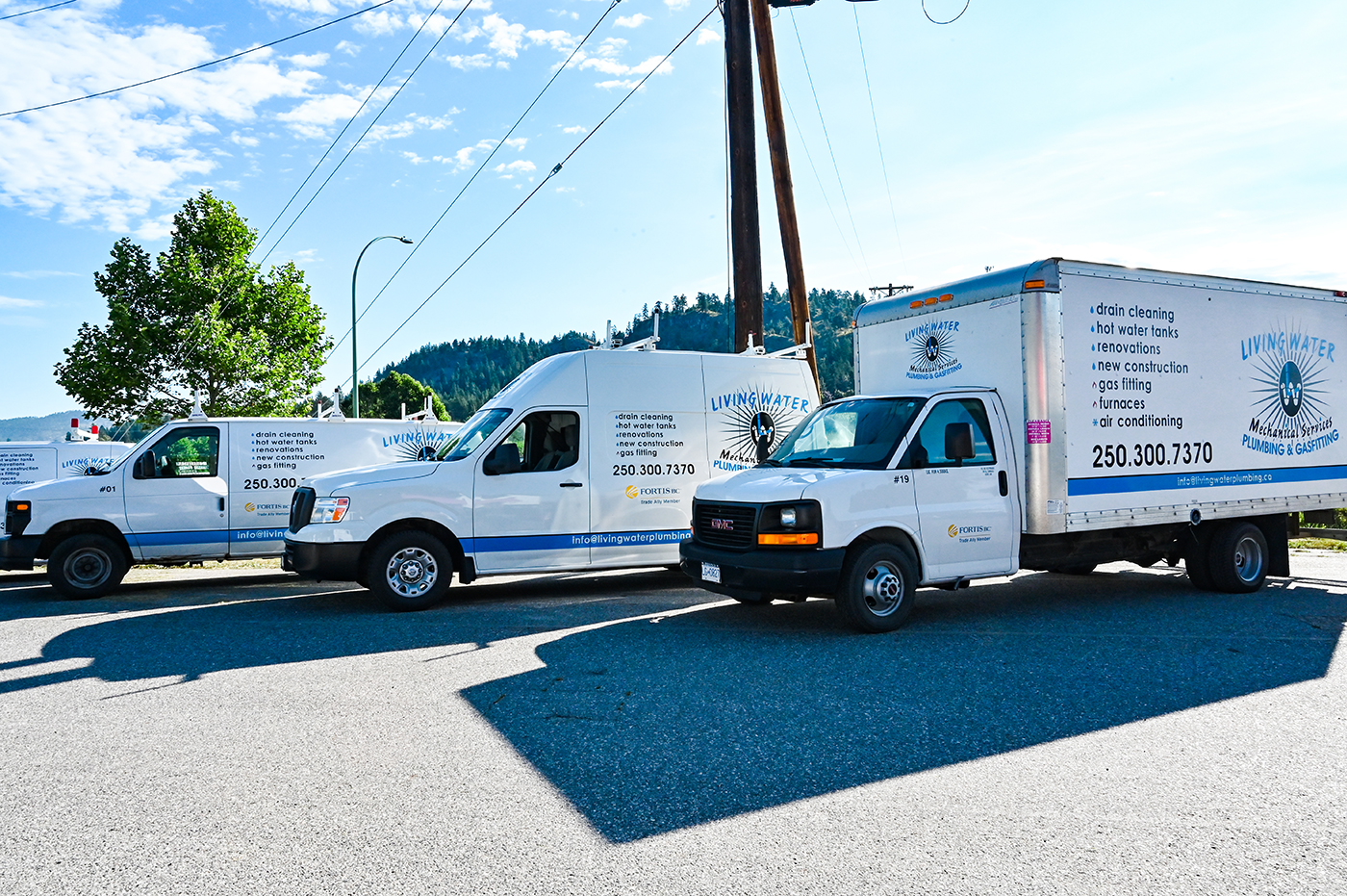 Three service trucks parked on a street, displaying the "Living Water Plumbing & Gasfitting" logo and services such as drain cleaning and air conditioning.