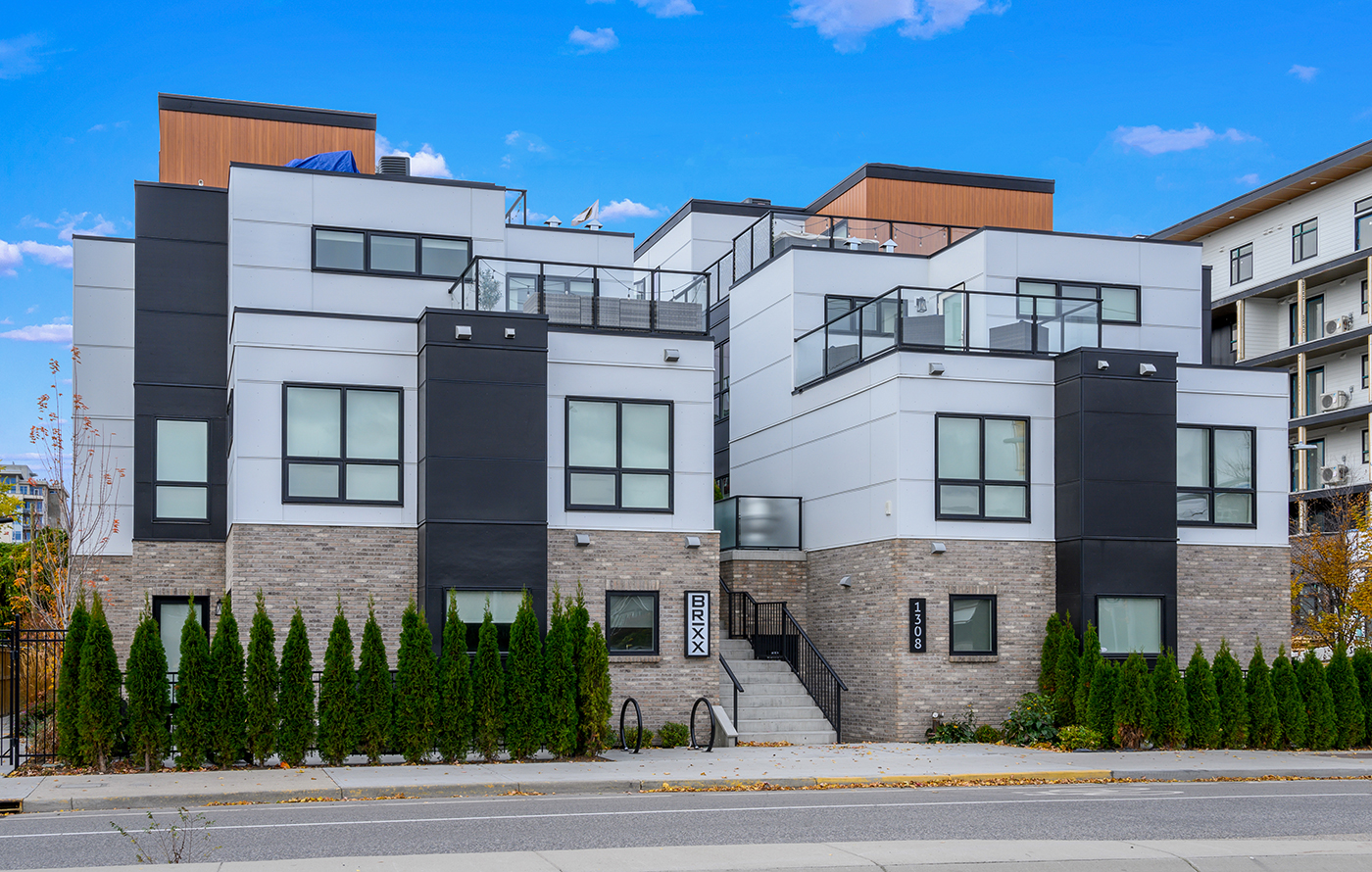 A modern multi-unit residential building with a mix of gray and black exterior, large windows, and a rooftop terrace.