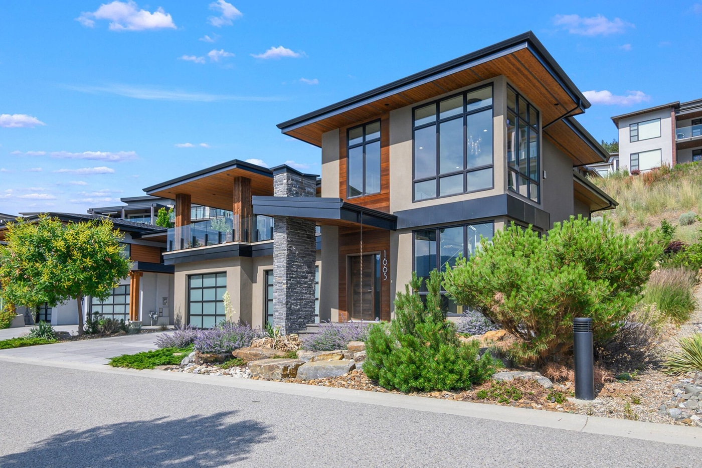 A modern two-story house with large windows, a stone accent wall, and a landscaped front yard.