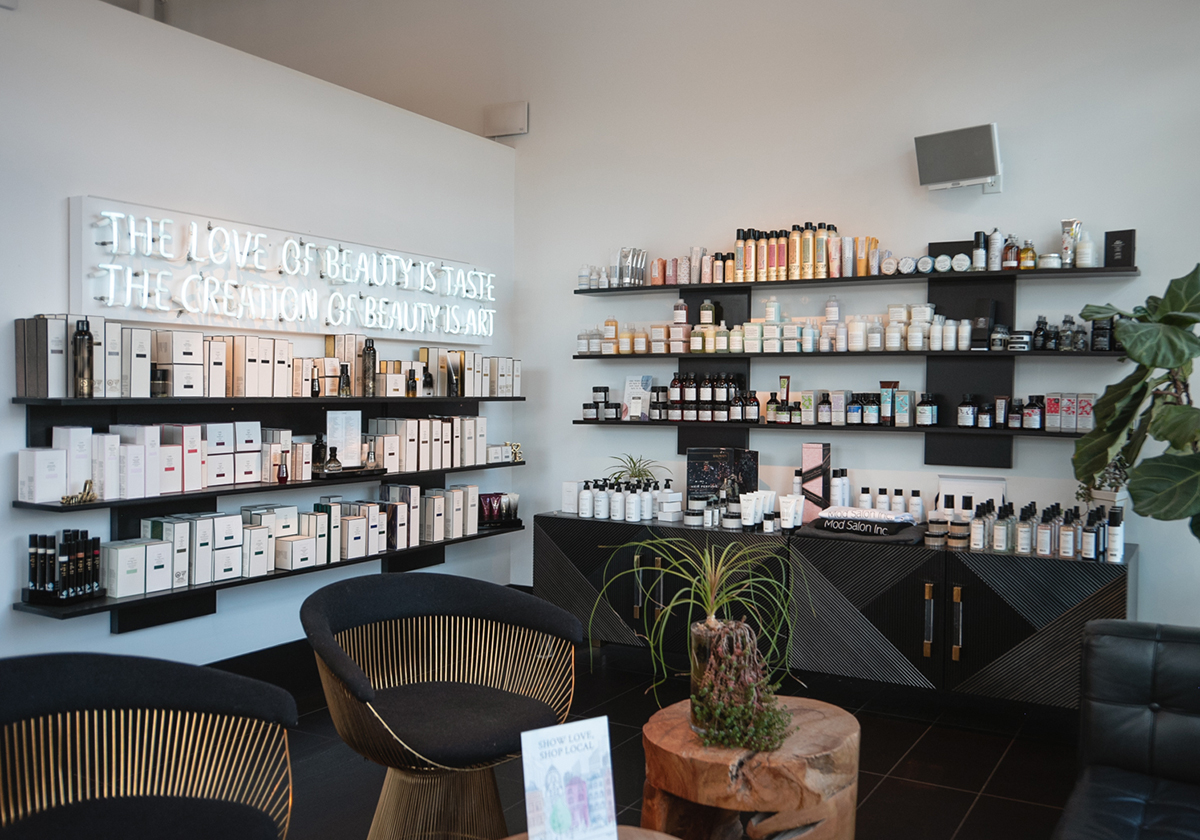 A modern beauty salon interior showcasing shelves filled with various skincare and cosmetic products, a neon sign, and stylish seating.