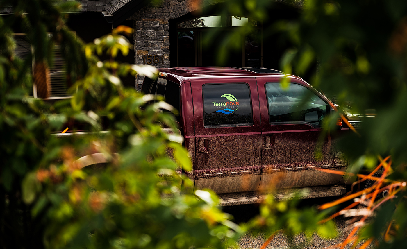 A maroon truck with a "Terranova Landscaping" logo, partially obscured by green foliage.