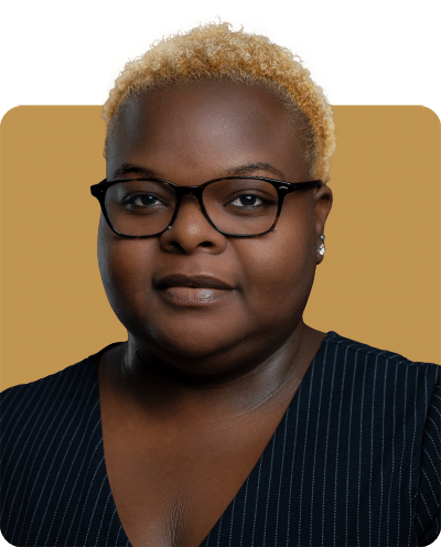 A portrait of a woman with short blonde hair and glasses, wearing a dark striped top, against a solid background.