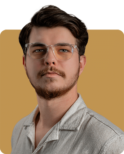 A young man with glasses and a facial beard, wearing a light-colored shirt, posed against a two-tone background.