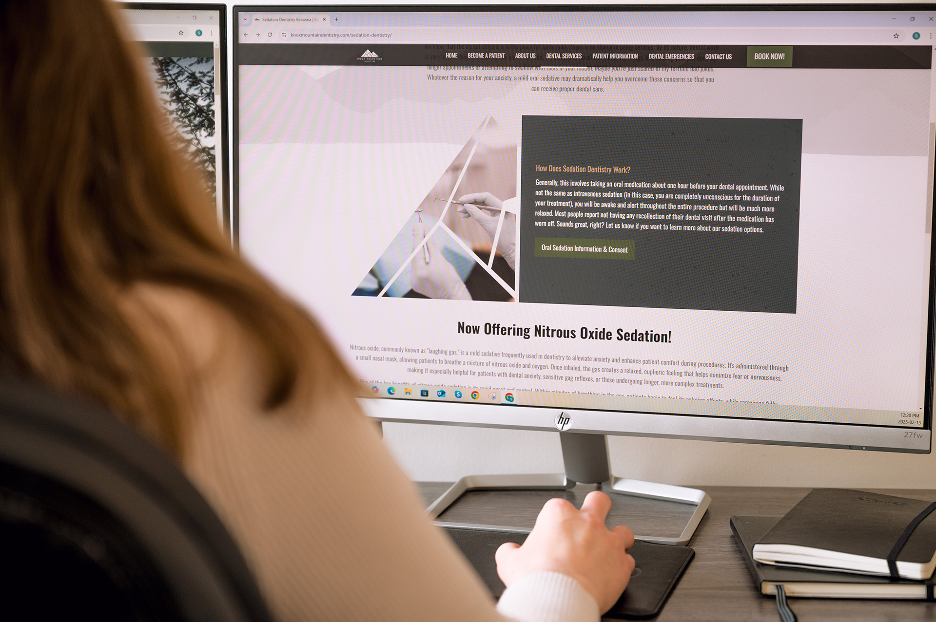 A person sitting at a desk is using a computer to read about nitrous oxide sedation on a dental website.