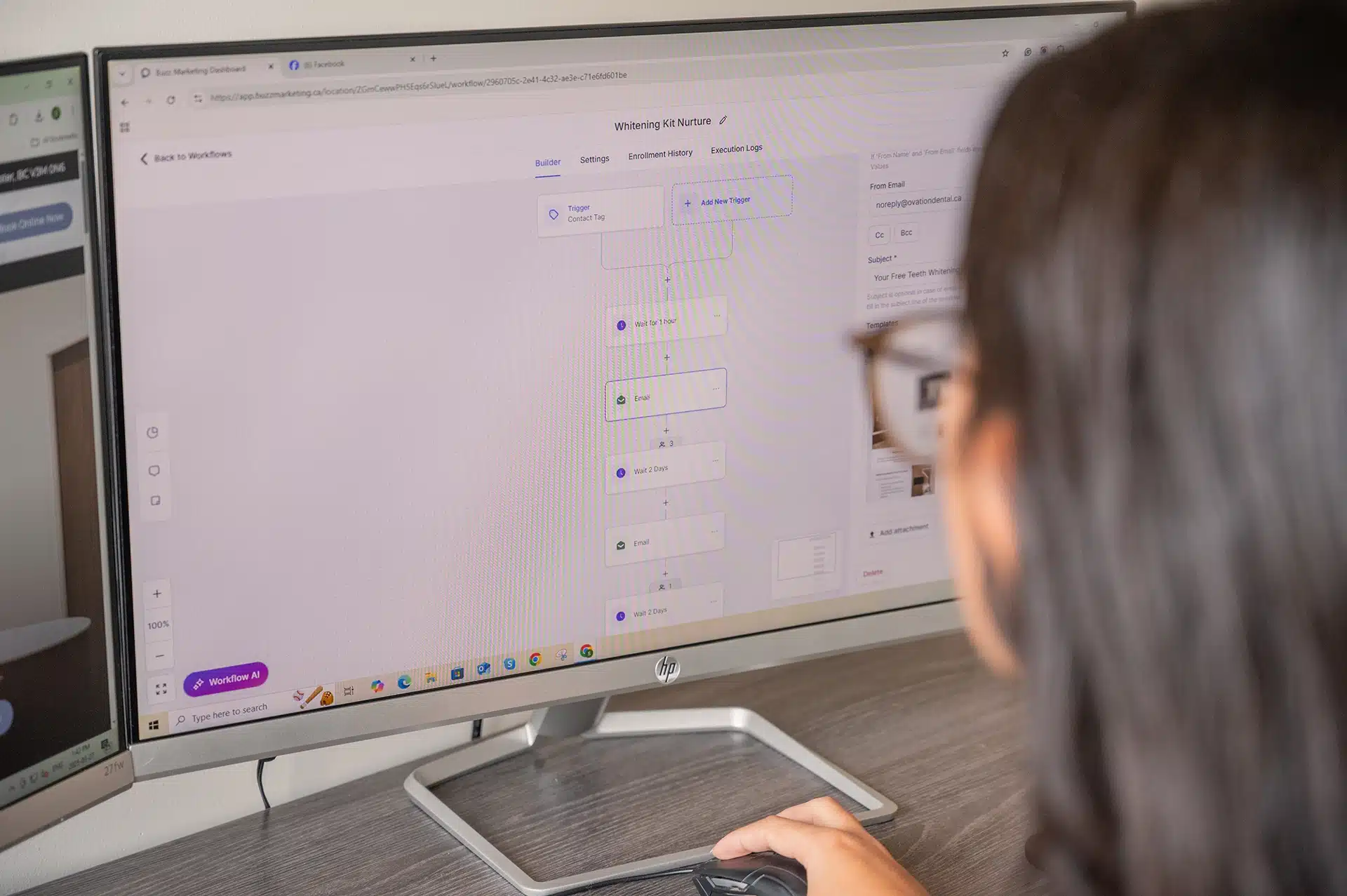 A person is using a computer to view a workflow interface on a large monitor, with elements related to email marketing and triggers visible on the screen.
