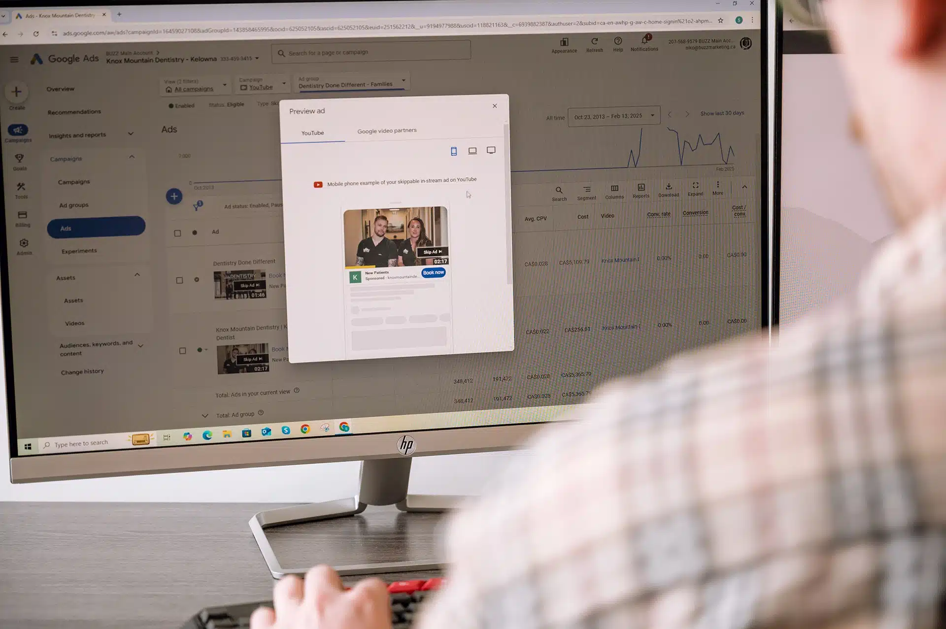 A person is using a computer to preview a YouTube advertisement for a dental practice, displayed on a screen with campaign data visible.