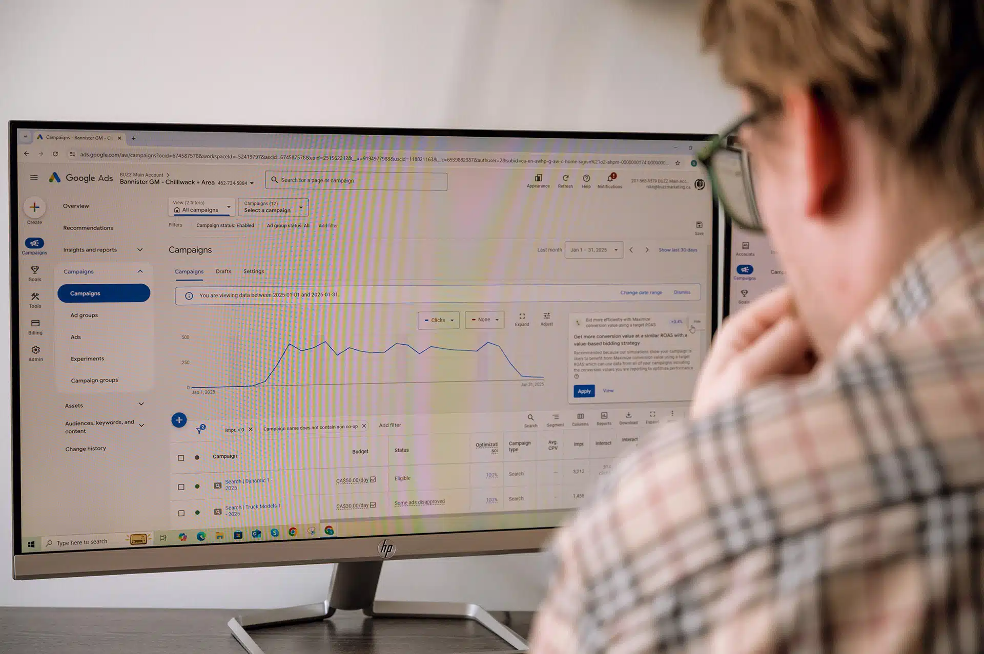 A person is looking at a computer screen displaying Google Ads campaign data, including graphs and metrics related to clicks and budget.