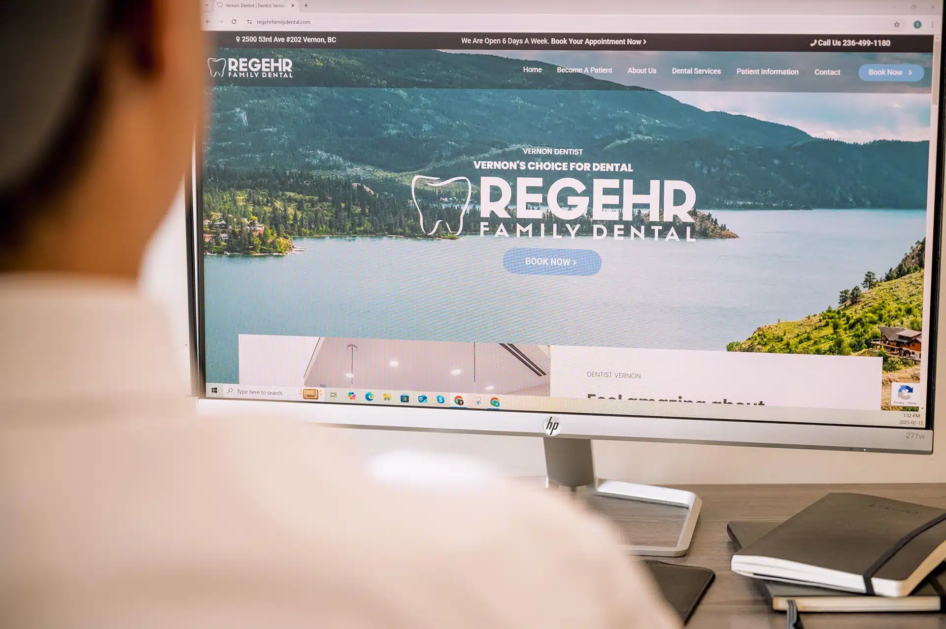 A person is viewing the website for Regehr Family Dental on a computer monitor, showing scenic views and dental service information.