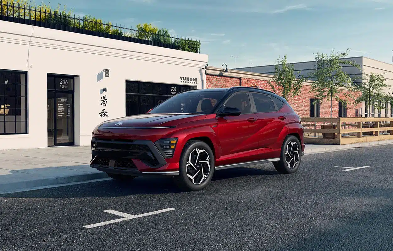 A red SUV parked on a street beside a building with large windows and a brick wall.