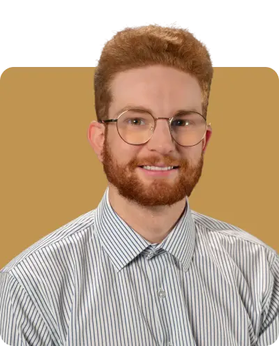 Head-and-shoulders portrait of a young man with a short beard and curly hair, wearing round glasses and a striped button-down shirt, posed against a neutral light brown background